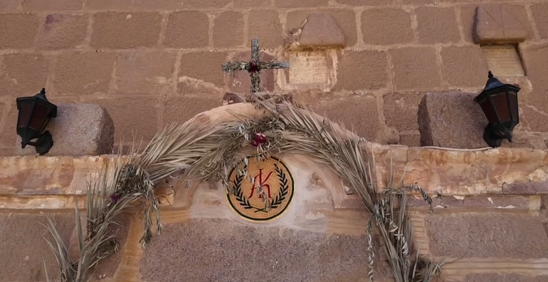 A cross and palm leaves on a stone wall

AI-generated content may be incorrect.